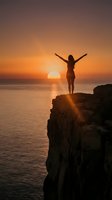 Woman with arms raised standing on rocky cliff overlooking ocean at sunset, celebrating freedom and achievement with golden sky and calm water below.