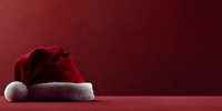 Traditional red Santa Claus hat with white fur trim on burgundy background, festive holiday concept for Christmas season designs.