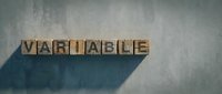 Wooden letter blocks spelling VARIABLE on concrete surface with dramatic shadow, representing adaptability and flexibility in business concepts.