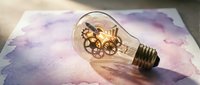 Vintage light bulb with brass gears and clockwork mechanism inside on purple watercolor background. Creative steampunk innovation concept for business ideas.