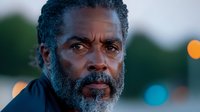 Senior African American man with gray beard looking thoughtfully into distance against blurred bokeh lights background, emotional portrait capturing wisdom and life experience.