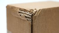 Damaged brown cardboard shipping box with torn corner showing wear from handling and transportation for packaging concepts.