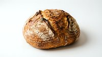 Freshly baked artisan sourdough bread loaf with crispy golden crust and flour dusting, isolated on white background for bakery, food, and culinary design projects.