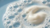 Creamy white foam with bubbles floating on light blue water surface creating abstract texture for spa wellness and cleaning product concepts.