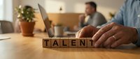 Business professional arranging wooden letter blocks spelling TALENT on office desk during recruitment meeting for human resources and career development.