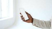 Close-up of male hand holding blank white smartphone with empty screen against bright window background for app mockup and mobile technology display.