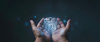 Hands holding glowing shield icon representing cybersecurity, data protection, and digital safety for technology and business applications.