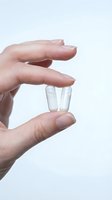 Hand holding two white capsules pills between fingers on clean white background for healthcare and medicine concepts.