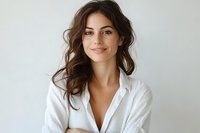 Young woman with natural makeup and wavy brown hair wearing white button-up shirt smiling confidently against light background. Professional portrait capturing genuine expression.