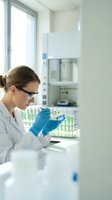Female scientist in white lab coat examining plant sample in test tube wearing safety glasses and blue gloves in modern laboratory for research and development.