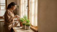 Woman watering potted plants on windowsill in natural sunlight, indoor gardening and home plant care concept.