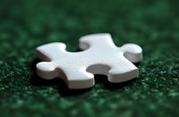 Single white jigsaw puzzle piece on green textured background with shallow depth of field, representing solutions, strategy and business concepts.