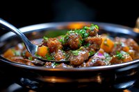 Savory meatballs with vegetables in rich brown sauce garnished with fresh herbs, served in black pan. Close-up view shows juicy texture and appetizing glaze.