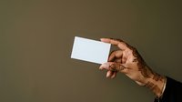 Tattooed hand holding blank white card against neutral background for branding and marketing purposes.