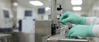 Laboratory technician in green gloves operating precision equipment in sterile pharmaceutical manufacturing facility for quality control testing.