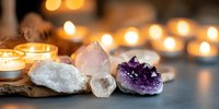 Healing crystals and burning candles create spiritual atmosphere with amethyst, rose quartz and clear quartz on dark surface with soft bokeh lights in background.