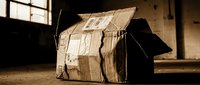 Cardboard house model made from recycled boxes in rustic warehouse setting with natural window lighting for creative play and imagination concepts.