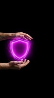 Hands holding glowing neon shield symbol against black background. Magenta light represents security, protection, and digital safety for technology concepts.