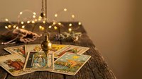 Mystical tarot cards spread on wooden surface with golden pendulum and warm fairy lights creating atmospheric fortune telling scene for spiritual guidance.