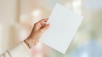 Hand holding blank white paper sheet against blurred background, suitable for mockups, presentations, and advertising campaigns.
