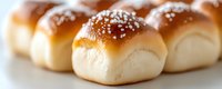 Fresh homemade dinner rolls with sea salt sprinkled on top, showing soft golden brown crust and fluffy texture in selective focus macro photography.