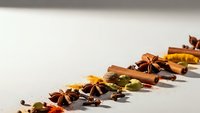 Autumn spices and colorful leaves arranged in decorative line on white background for seasonal cooking and holiday baking projects.