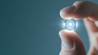 Glowing futuristic energy core held between fingers against teal background, radiating bright white light in circular pattern, symbolizing innovation and power.