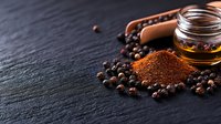 Ground black pepper powder and whole peppercorns with glass jar of olive oil on dark stone background, macro food photography with copy space.