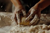 Hands kneading raw dough on wooden surface covered with flour, close-up view showing texture and baking process in warm natural lighting.