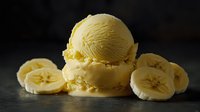 Creamy banana ice cream scoop on dark background with fresh banana slices, showcasing smooth texture and natural yellow color for food photography and menu design.