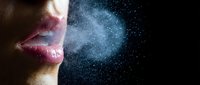 Woman exhaling breath vapor cloud with water droplets against dark background showing respiratory system and cold weather breathing effects.