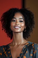 Young African American woman with curly afro hair smiling confidently in colorful floral dress against warm background for lifestyle and fashion content.