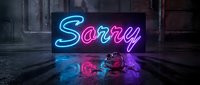 Glowing neon Sorry sign in pink and blue lights on wet dark floor with broken object, dramatic urban atmosphere for apology concepts.