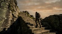 Male hiker with backpack exploring ancient stone ruins at dramatic sunset with golden sky and rocky landscape adventure travel concept.