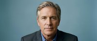 Mature male professional with gray hair and light complexion wearing dark blazer over blue shirt against neutral blue background for corporate portraits.