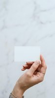 Hand holding blank white business card against marble background, ready for custom branding and contact information design.
