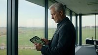 Senior Caucasian businessman reading digital tablet in modern office with panoramic windows overlooking countryside landscape during daytime.