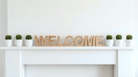Wooden welcome sign letters on white fireplace mantel surrounded by small potted cactus plants, minimalist home decor interior styling.