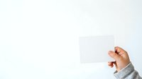 Hand holding blank white card against light background, suitable for business branding, marketing mockups, and promotional material presentations.