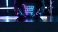 Hands holding glowing neon shopping cart symbol on dark surface with blue and purple light effects, representing digital commerce and online retail technology.