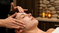 Young Caucasian woman receiving a relaxing facial massage with cream mask at a luxury spa, candles glowing in the background.
