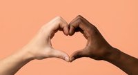 Two diverse hands forming heart shape symbol representing unity love and togetherness against coral background for social campaigns and diversity projects.