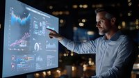 Mature Caucasian businessman analyzing financial charts and graphs on digital screen in dark office. Data visualization and market analysis concept for finance sector.