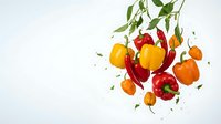 Fresh colorful bell peppers with green leaves falling and floating on white background, isolated organic vegetables for healthy cooking and nutrition.