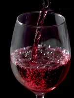 Red wine pouring into glass with bubbles and splash against black background for beverage and dining concepts.
