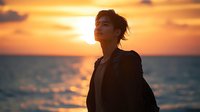 Young Asian man in business attire silhouetted against dramatic orange sunset over ocean, eyes closed in peaceful moment of reflection and mindfulness.