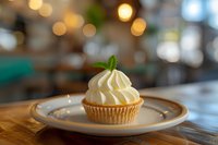 Vanilla cupcake topped with swirled buttercream frosting and fresh mint leaf garnish on ceramic plate against soft bokeh background, food photography styling.