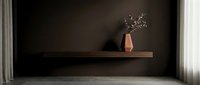 Minimalist interior with wooden floating shelf displaying terracotta vase and dried flowers against dark wall, modern home decor and design inspiration.