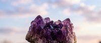 Purple amethyst crystal cluster against soft pastel sky background for meditation, healing and spiritual wellness concepts.
