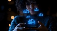 Glowing blue holographic houses floating above hands in dark setting with bokeh lights, representing smart home technology and digital real estate innovation.